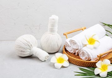 Spa massage Aromatherapy body care background. Spa herbal bags, towel and tropical flowers on gray concrete table. copy space. Beauty and health care concept